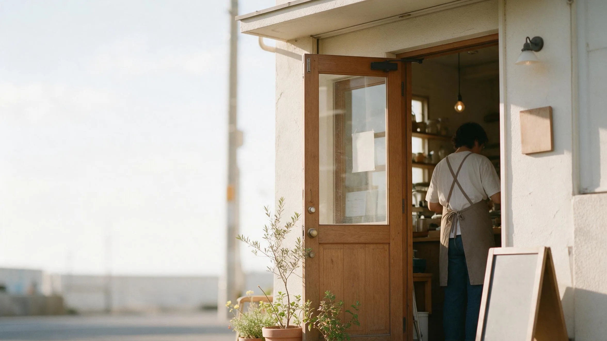 夕方の光が入る小さなお店の入り口で、店主が奥で作業している様子